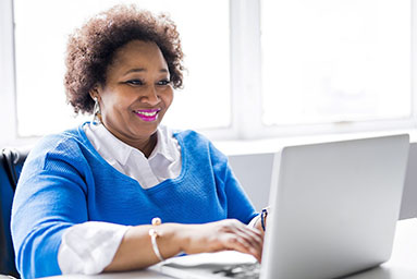 A smiling Black woman sitting and typing at a laptop.